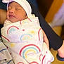 newborn, baby, sleeping, blanket, rainbow_pattern, headband, flower, swaddled, infant, person, indoor, soft, cute, peaceful, resting, hand, comfort, warm, closeup, portrait