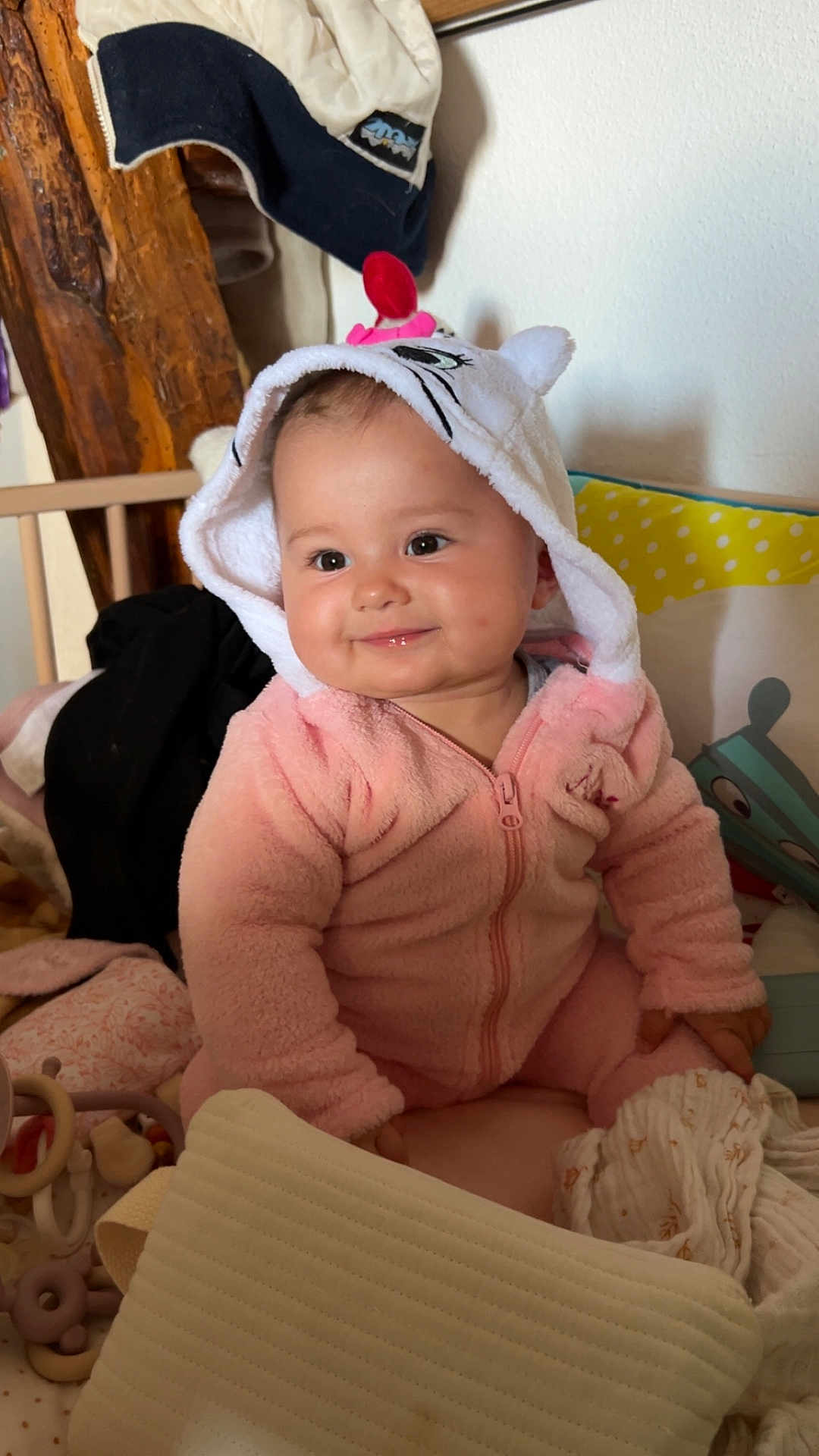 Maëlys Bodein a rejoint le concours — aidez-le/la à gagner de superbes lots ! baby, child, pink_onesie, hood, smile, indoor, soft_toys, blanket, cozy, cute, face, infant, seated, wooden_furniture, pillow, play_area, warm_lighting, home, young_child, adorable