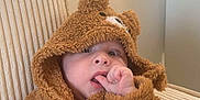 Elyas participe au concours pour gagner de l'argent avec cette photo : baby, child, fuzzy_clothing, bear_costume, thumb_sucking, indoor, chair, cute, cozy, infant, portrait, soft_texture, beige, comfortable, close_up, expression, young_child, seated, hood, person