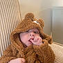 baby, child, fuzzy_clothing, bear_costume, thumb_sucking, indoor, chair, cute, cozy, infant, portrait, soft_texture, beige, comfortable, close_up, expression, young_child, seated, hood, person