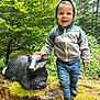 child, toddler, hoodie, jeans, smiling, badger_statue, moss, tree_stump, forest, nature, outdoor, greenery, shoes, person, happy, daylight, casual_clothing, wood, foliage, cute