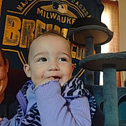 Athena is registered to the contest to win money with this photo: toddler, child, smiling, purple_clothing, indoor, cat_tree, banner, face, person, sleeve, furniture, window, light, hand, jacket, happy, playful, portrait, baby, home