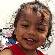 Na'Son is registered to the contest to win money with this photo: bedroom, camera, casual, child, close_up, clothing, door, face, happy, home, indoors, long_hair, messy_hair, person, playful, portrait, red_shirt, sitting, smiling, toddler