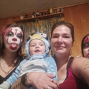 Summer is registered to the contest to win money with this photo: baby, face_paint, clown_makeup, costume, family, portrait, indoor, wood_paneling, curtains, smile, tongue_out, person, tattoo, watch, necklace, shelf, figurines, casual_clothing, child, holding