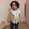 child, toddler, portrait, standing, curly_hair, jacket, coat, shearling, white_shirt, jeans, boots, shoes, indoor, fashion, fashionable, floor, wall, curtain, full_body, serious_expression