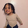 Adonis is registered to the contest to win money with this photo: child, toddler, smiling, portrait, curly_hair, standing, indoors, pink_wall, long_sleeves, shirt, pants, clothing, person, face, hair, happy, photography, home, casual, pose