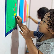 Adonis is registered to the contest to win money with this photo: child, toddler, curly_hair, profile, smiling, focused, indoor, classroom, learning, education, activity, wall_board, shapes, stickers, colorful, hands, creative, second_child, portrait, photography