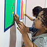 child, toddler, curly_hair, profile, smiling, focused, indoor, classroom, learning, education, activity, wall_board, shapes, stickers, colorful, hands, creative, second_child, portrait, photography