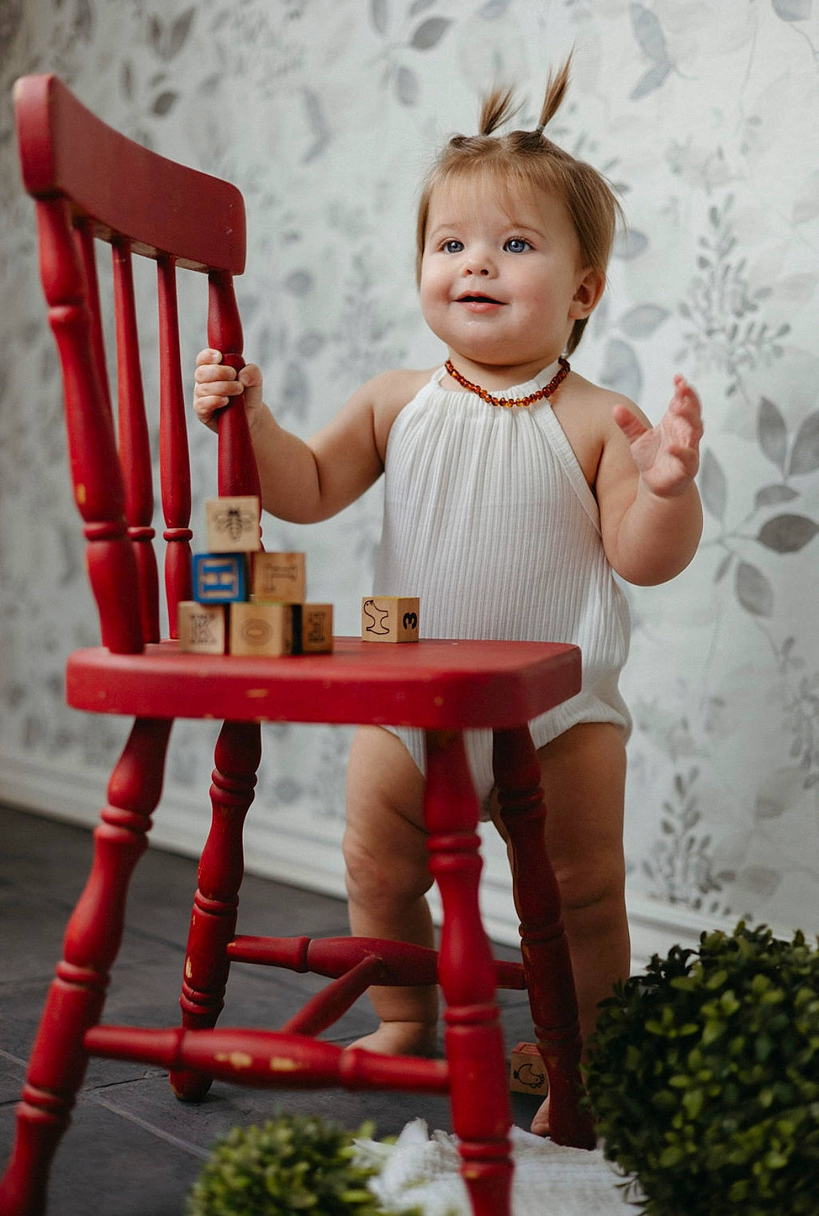 Oakley is registered to the contest to win money with this photo: baby, baby_toddler_clothing, chair, face, furniture, happy, head, human_body, joint, leg, outdoor_furniture, person, plant, shorts, sleeve, smile, standing, table, textile, toddler