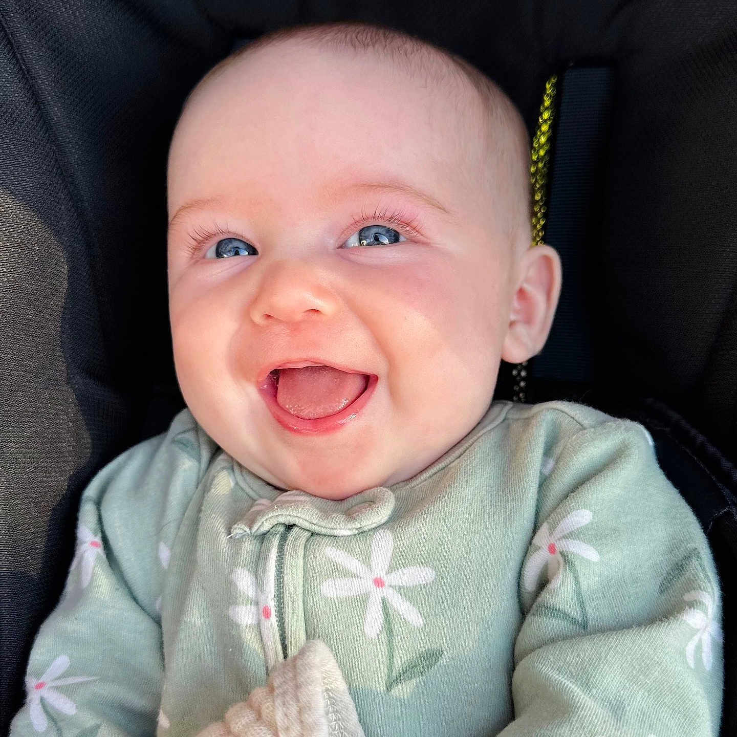 Julia is registered to the contest to win money with this photo: baby, smiling, blue_eyes, infant, green_clothing, daisy_pattern, happy, cute, portrait, close_up, child, face, soft_lighting, cozy, young_child, adorable, seated, fabric, blanket, innocence