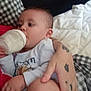 Jamalakai is registered to the contest to win money with this photo: baby, bottle, feeding, tattoo, arm, hand, bed, blanket, checkered_pattern, clothing, infant, person, skin, resting, comfort, indoor, closeup, holding, sleepwear, relaxation