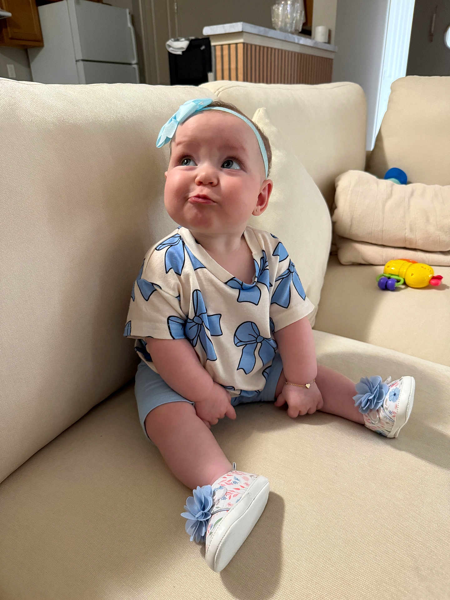 Ashley is registered to the contest to win money with this photo: baby, child, infant, couch, sofa, headband, blue_bow, shoes, floral_shoes, flower, bracelet, cute, sitting, indoor, living_room, toy, pillow, expression, clothing, person