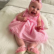 Ashley joined the competition — help win amazing prizes! baby, child, pink_dress, headband, bow, smile, laughing, bed, blanket, white, footwear, shoes, cute, indoors, portrait, happy, toddler, infant, clothing, person