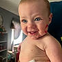 baby, child, smiling, face, blue_eyes, lipstick_mark, diaper, skin, arm, hand, indoor, window, curtain, furniture, shelf, person, happy, closeup, light, home