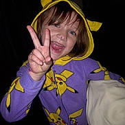 Arabella is registered to the contest to win money with this photo: child, smile, peace_sign, pajamas, pikachu, hoodie, blanket, indoor, happy, face, hand, purple, yellow, clothing, person, cute, portrait, night, fun, gesture