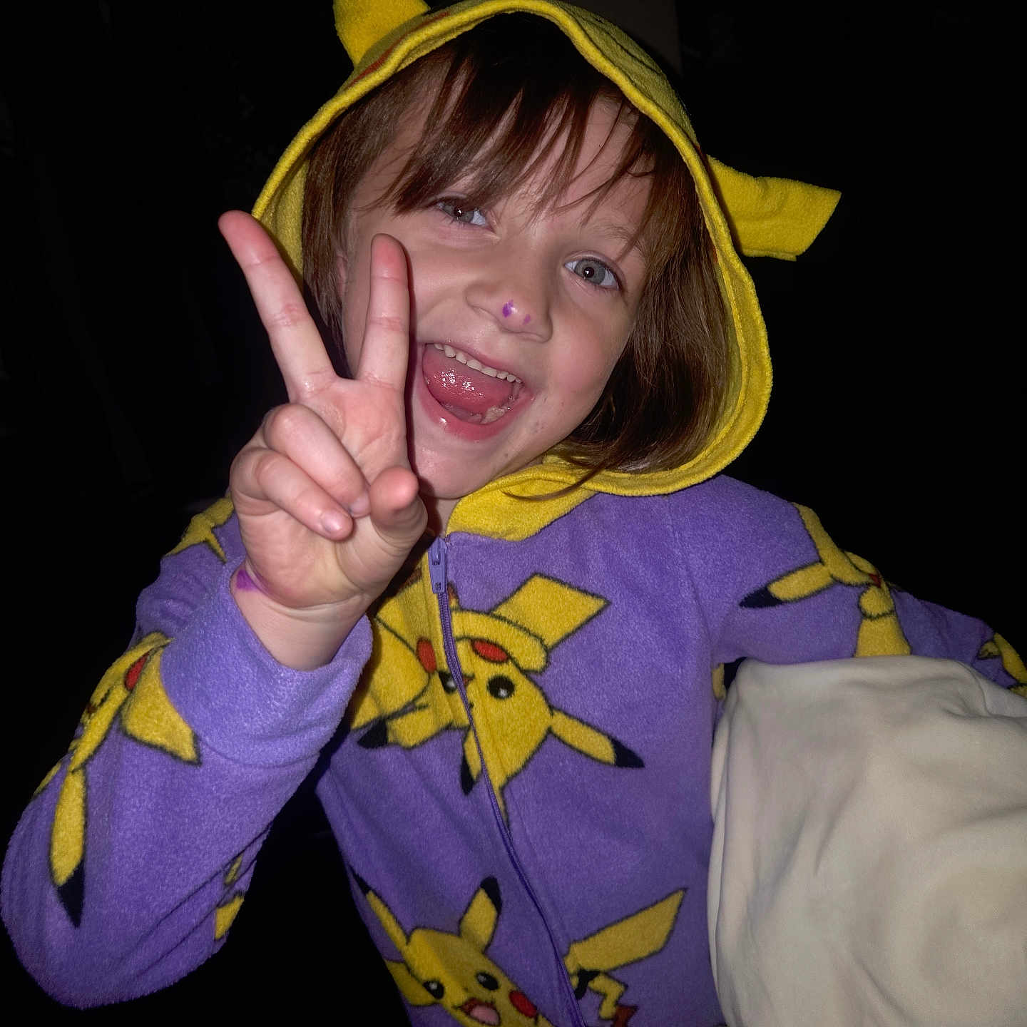 Arabella is registered to the contest to win money with this photo: blanket, child, clothing, cute, face, fun, gesture, hand, happy, hoodie, indoor, night, pajamas, peace_sign, person, pikachu, portrait, purple, smile, yellow