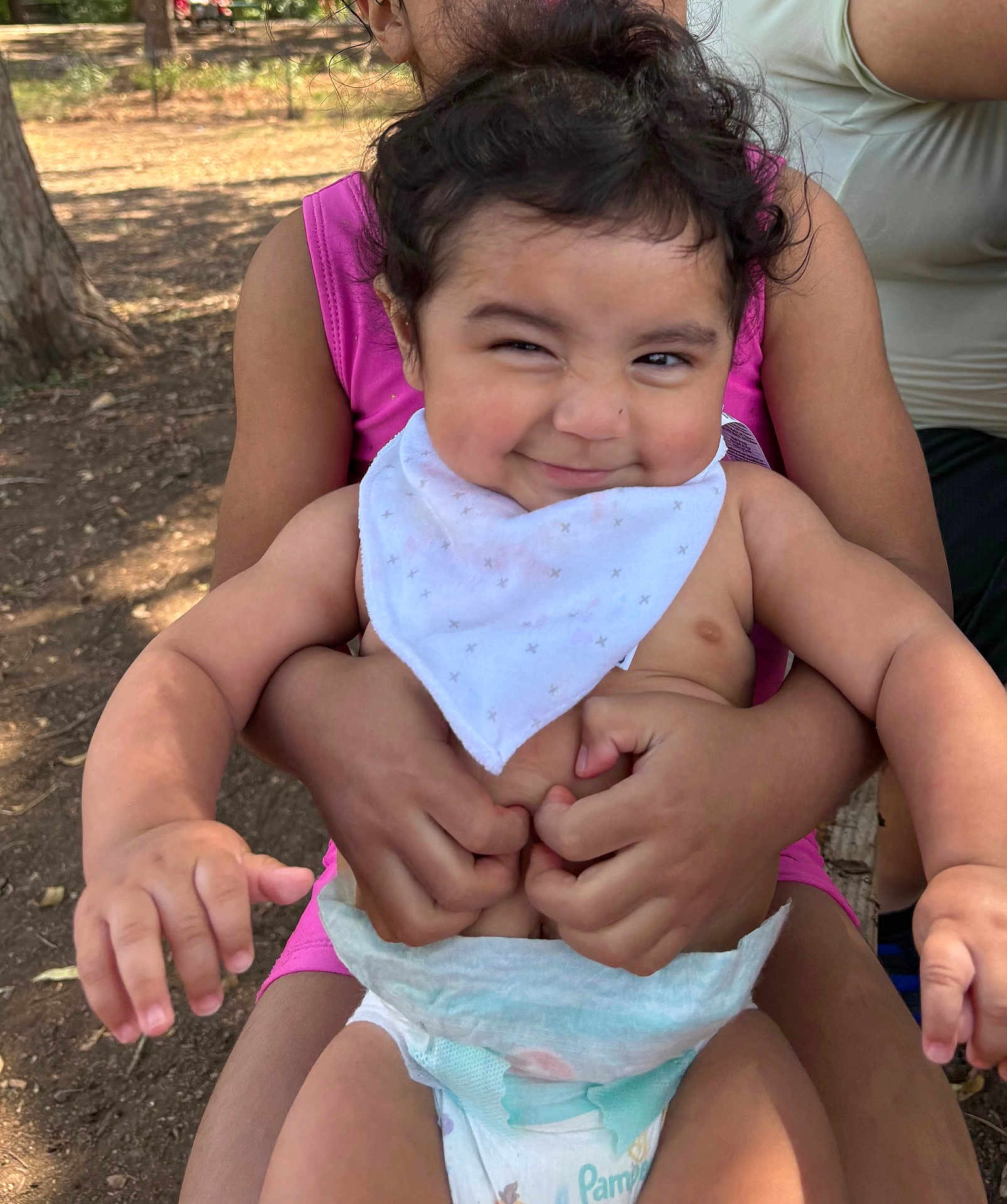 Leandro is registered to the contest to win money with this photo: baby, child, outdoor, smile, diaper, bib, holding, person, nature, tree, sunlight, face, happy, skin, arm, hand, pink_clothing, playing, candid, portrait