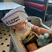 Noah joined the competition — help win amazing prizes! baby, high_chair, paper_hat, diner, smiling, stuffed_animal, tiled_floor, booth_seating, child, clothing, indoor, table, cute, person, seatbelt, toy, restaurant, happy, headwear, infant