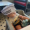 baby, high_chair, paper_hat, diner, smiling, stuffed_animal, tiled_floor, booth_seating, child, clothing, indoor, table, cute, person, seatbelt, toy, restaurant, happy, headwear, infant