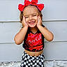 toddler, child, smiling, red_bow, coca_cola, checkered_shorts, happy, portrait, outdoor, standing, hands_on_face, cute, fashion, headband, wall, stone, background, person, apparel, expression