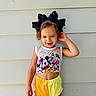 toddler, child, smiling, standing, mickey_mouse, crop_top, shorts, yellow_shorts, black_bow, hair_bow, cute, happy, playful, wall, outdoor, summer_clothing, fashion, portrait, person, casual