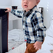 Elijah joined the competition — help win amazing prizes! toddler, child, plaid_shirt, brown_pants, sneakers, bed, playpen, indoor, curly_hair, standing, person, white_bed, clothing, footwear, home, young_child, expression, grip, casual, cute