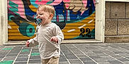 Amaë a rejoint le concours — aidez-le/la à gagner de superbes lots ! building, cartoon, child, cobblestone, dog, door, graffiti, long_sleeve_shirt, mural, outdoor, pacifier, playful, shorts, smiling, sneakers, street, toddler, urban_art, walking, wall
