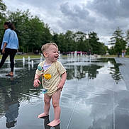 Amaë participe au concours pour gagner de l'argent avec cette photo : barefoot, casual_clothing, child, cloudy_sky, fountain, grass, happy, laughing, nature, outdoor, pacifier_clip, park, person, play, reflection, summer, toddler, trees, water, young