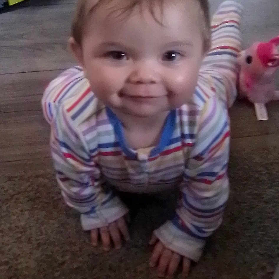 Bethany joined the competition — help win amazing prizes! baby, carpet, child, crawling, curious, cute, face, floor, footwear, home, indoor, infant, person, pink_toy, playful, smiling, sneaker, striped_pajamas, toy, wooden_floor