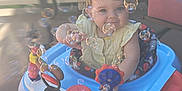 Bethany is registered to the contest to win money with this photo: baby, walker, bubbles, outdoor, porch, toy, child, smiling, face, seat, colorful, plastic, playful, greenery, sunlight, happy, person, young_child, blurred_background, disney