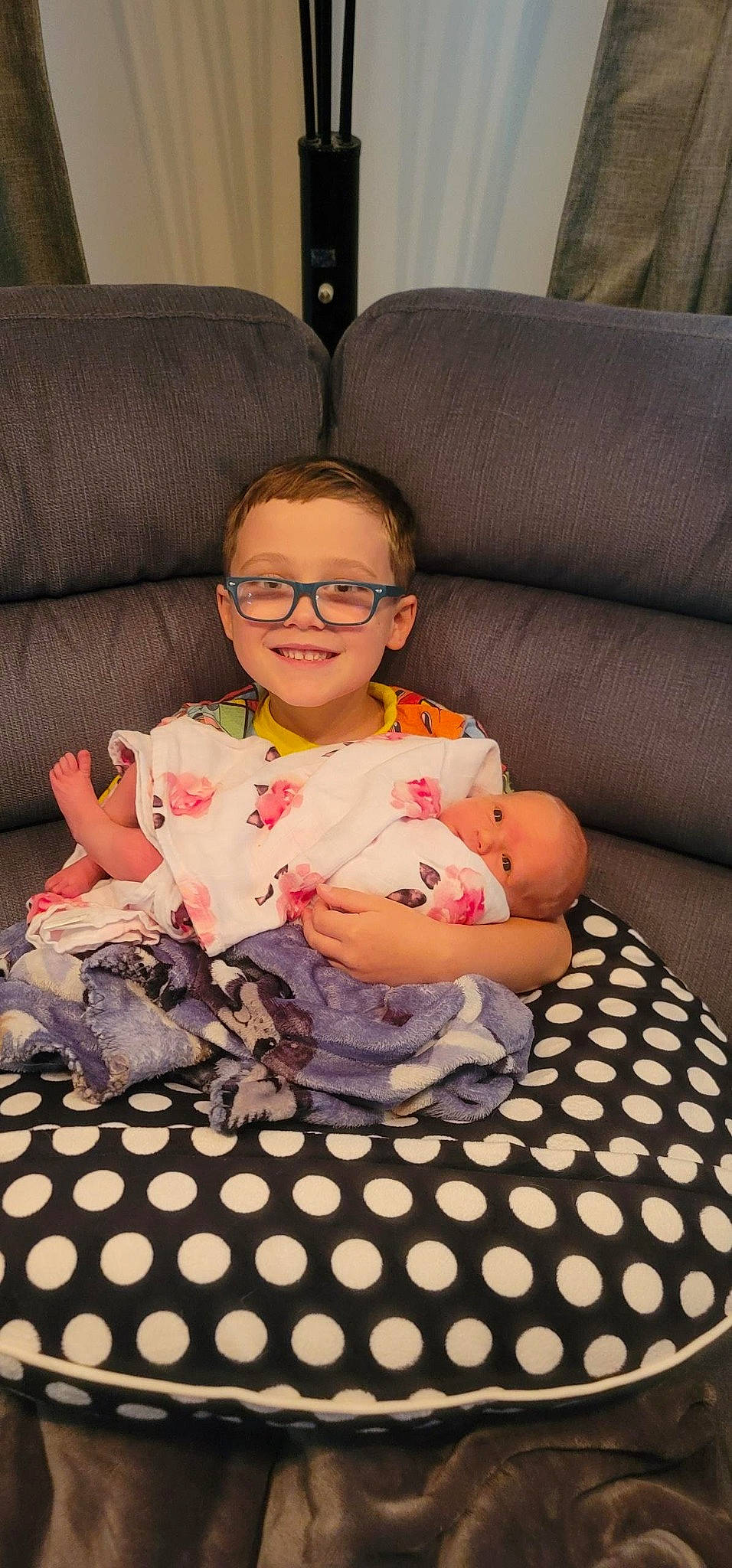 Connor is registered to the contest to win money with this photo: baby_toddler_clothing, cheek, child, comfort, couch, eyewear, finger, flooring, fun, glasses, happy, head, joy, lap, living_room, person, sitting, skin, smile, textile