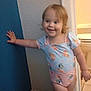 bathroom, blond_hair, carpet, casual_pose, child, doorway, floor, hand_on_wall, happy, home_interior, indoor, light, onesie, person, playful, smiling, standing, toddler, wall, young_child