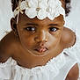 baby, child, portrait, face, headband, white_dress, curly_hair, close_up, cute, innocence, looking_up, adorable, fashion, studio, soft_lighting, expression, young_child, skin, person, beauty