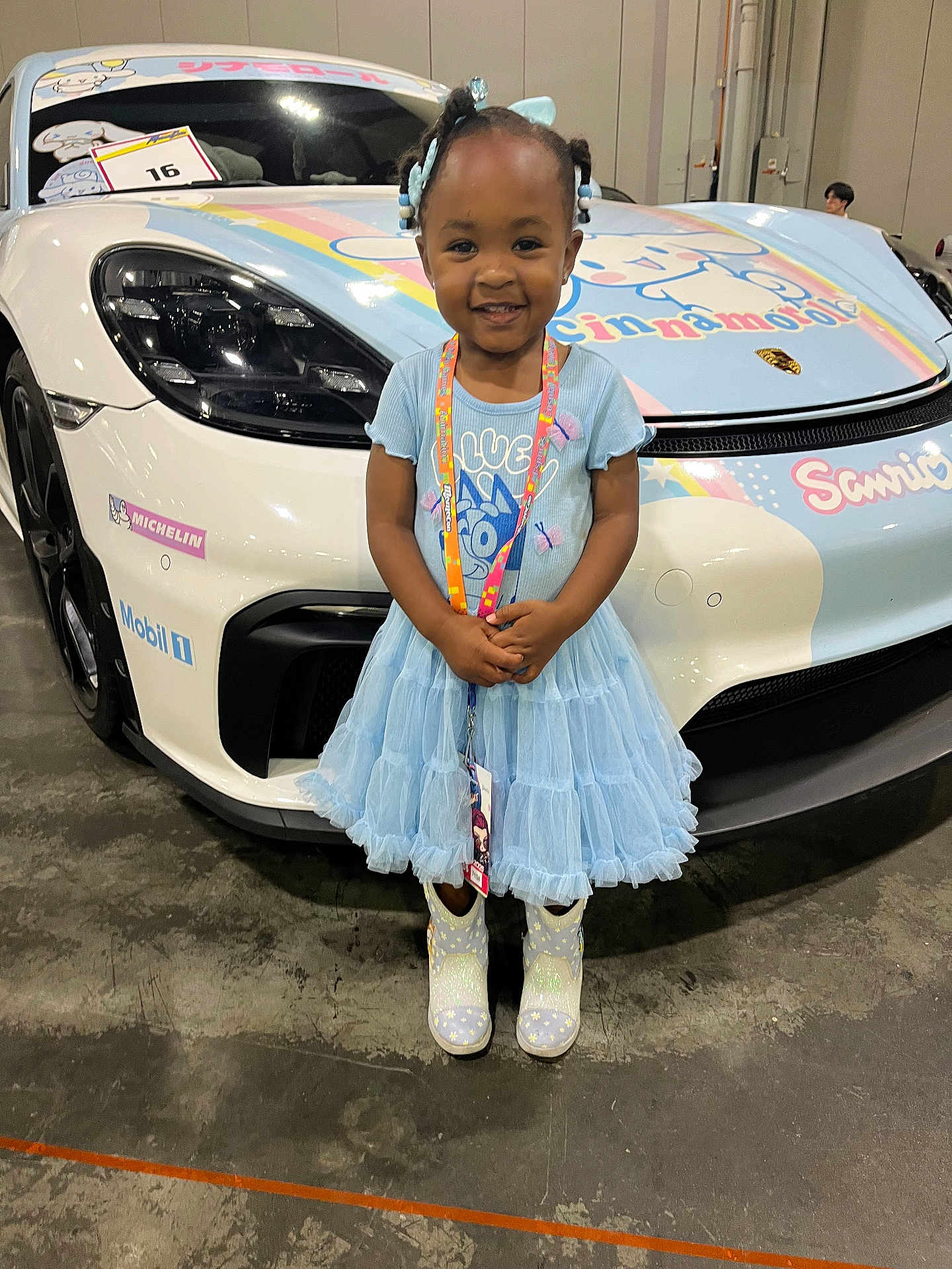 Diana joined the competition — help win amazing prizes! child, girl, blue_dress, sparkly_boots, smiling, standing, sports_car, white_car, cartoon_decorations, indoors, convention_center, lanyard, hair_bows, cute, happy, floor, license_tag, head, face, event