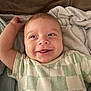 Grayson joined the competition — help win amazing prizes! baby, smiling, infant, face, tongue_out, arm_raised, blanket, soft_texture, checkered_shirt, clothing, lying_down, happy, cute, child, skin, head, person, indoors, cozy, portrait