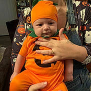 Grayson joined the competition — help win amazing prizes! baby, pumpkin_costume, orange_clothing, halloween, infant, child, adult, holding, portrait, indoor, casual, cute, costume, festive, smile, face, person, hand, overalls, fun