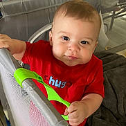 Grayson is registered to the contest to win money with this photo: baby, child, red_shirt, hug_text, playpen, green_handle, curious_look, indoor, blanket, soft_lighting, face, hand, cute, toddler, infant, smile, young_child, holding, home, portrait