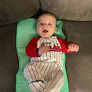 Grayson joined the competition — help win amazing prizes! baby, infant, child, couch, changing_pad, red_clothing, striped_pants, socks, face, person, indoor, smiling, happy, furniture, wood_floor, baby_outfit, cute, small_hands, lying_down, home