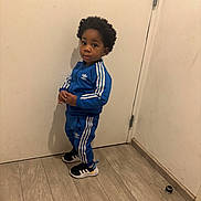 Kyzani a rejoint le concours — aidez-le/la à gagner de superbes lots ! child, toddler, blue_tracksuit, adidas, sneakers, standing, indoors, wooden_floor, door, curious_expression, black_hair, casual_clothing, sporty, young_person, full_body, portrait, floor, wall, footwear, person