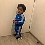 child, toddler, blue_tracksuit, adidas, sneakers, standing, indoors, wooden_floor, door, curious_expression, black_hair, casual_clothing, sporty, young_person, full_body, portrait, floor, wall, footwear, person
