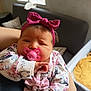 baby, pacifier, headband, floral_clothing, bow, infant, person, indoor, couch, window, arm, hand, sleepy, cute, soft_lighting, portrait, child, holding, cozy, newborn