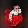 baby, sleeping, red_skirt, white_top, infant, child, cushion, dark_background, peaceful, portrait, indoor, cute, holiday, festive, clothing, young_child, resting, soft_lighting, adorable, small_hand