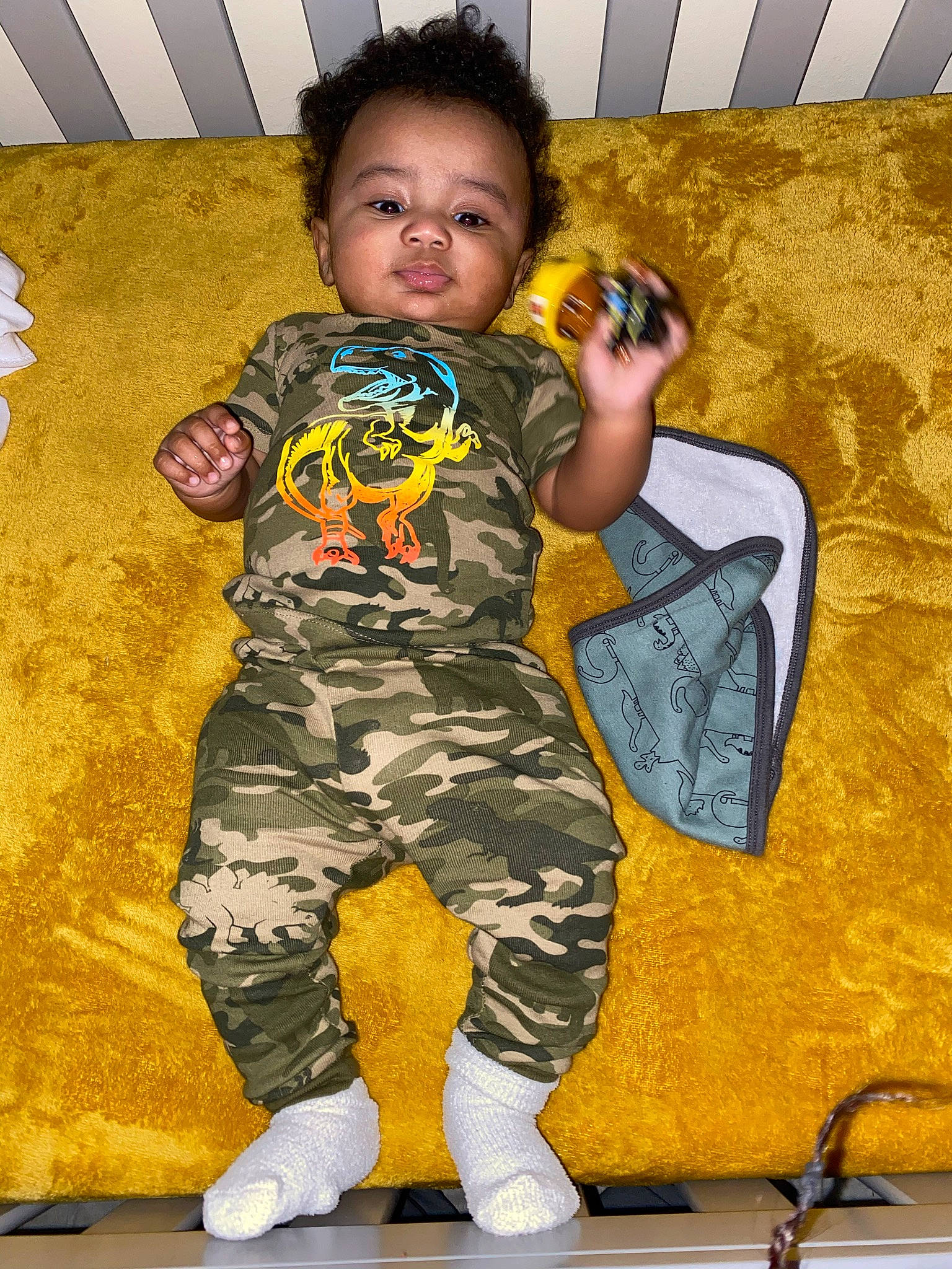 Travon is registered to the contest to win money with this photo: baby, baby_toddler_clothing, child, costume, fun, gesture, happy, human_leg, leg, military_camouflage, nightwear, orange, pajamas, pattern, person, play, sitting, sleeve, t_shirt, thigh