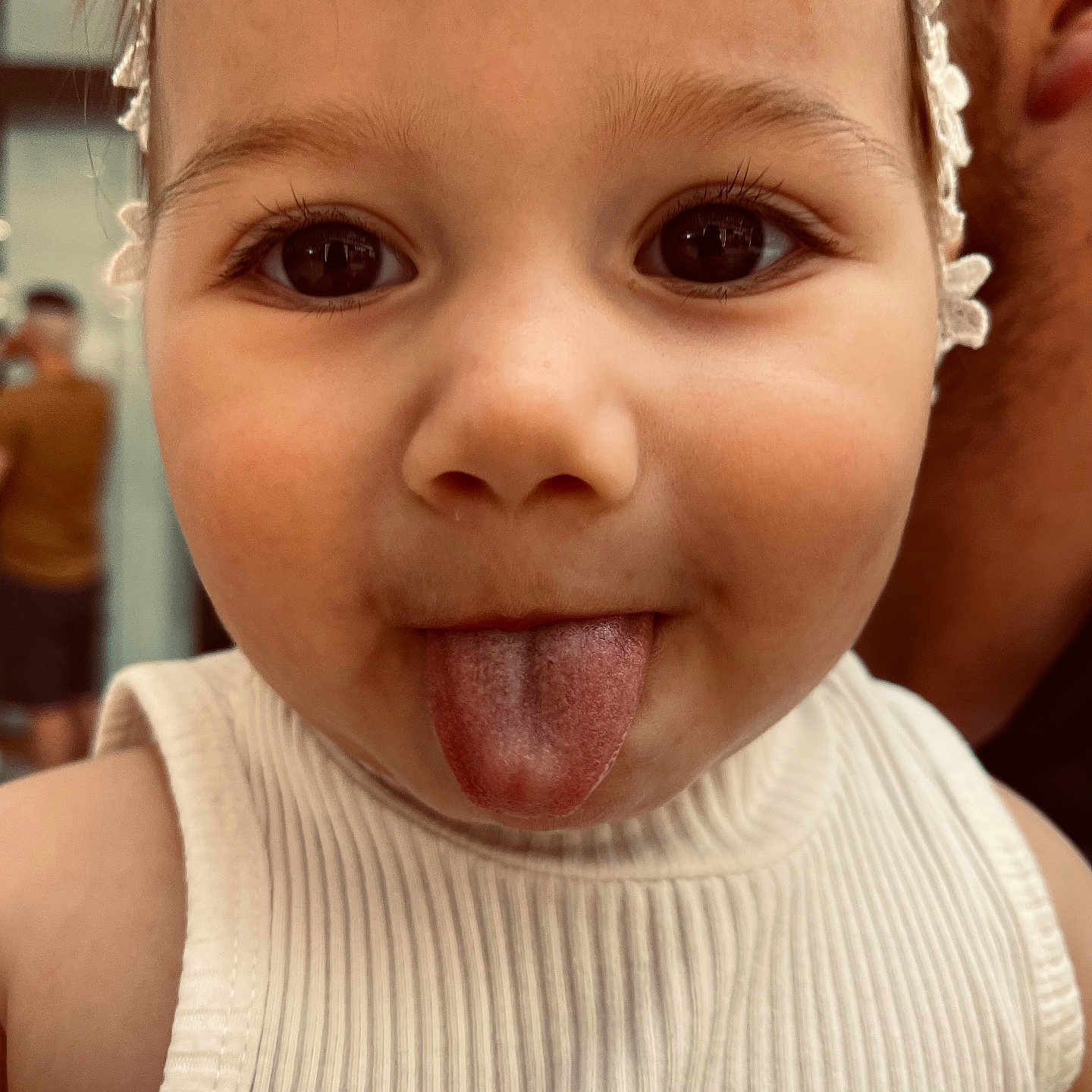 Hana is registered to the contest to win money with this photo: cheek, child, childhood, close_up, cute, expression, eyelashes, eyes, face, funny, headband, indoors, person, playful, portrait, skin, toddler, tongue, white_tank_top, young