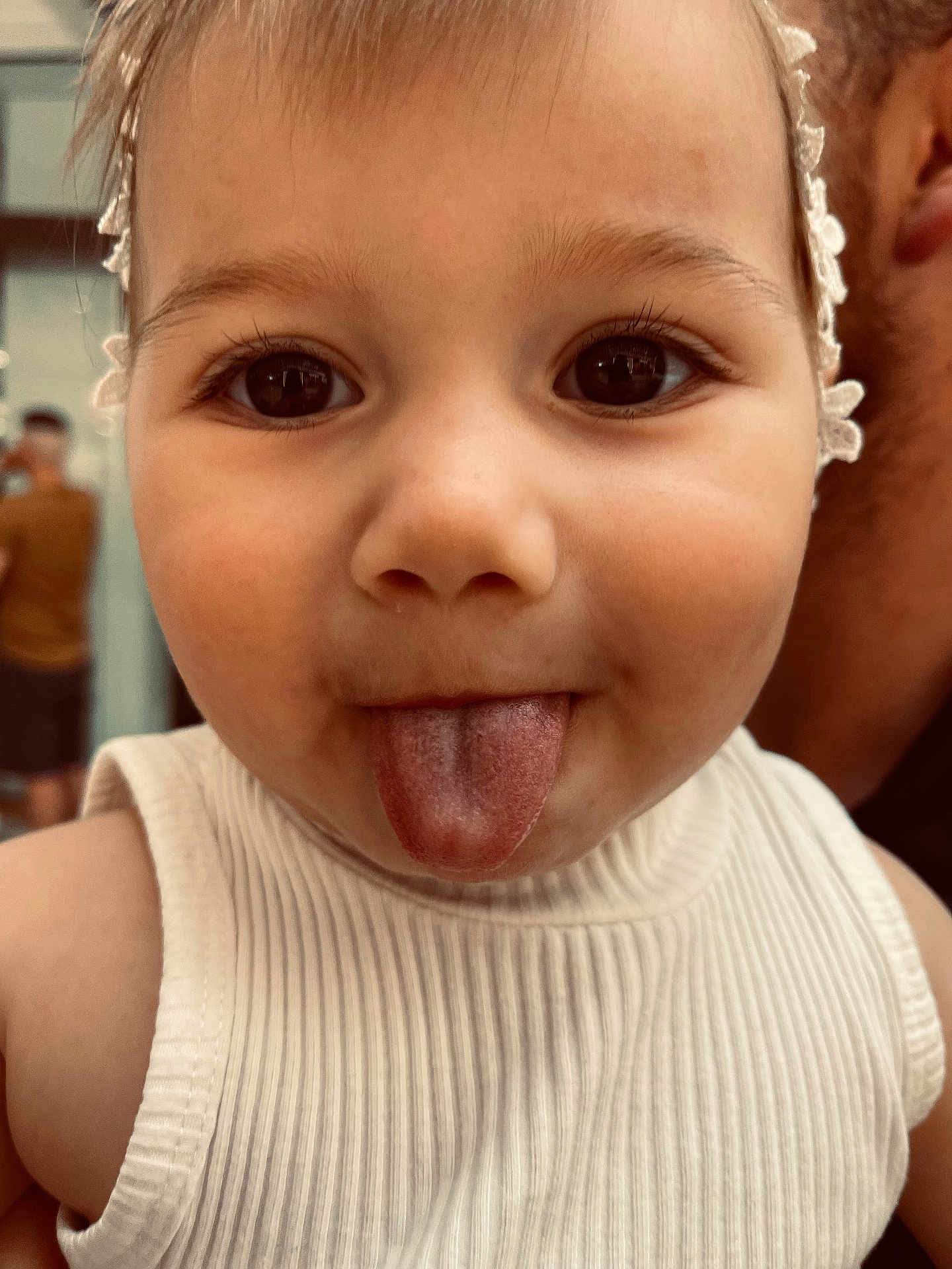 Hana is registered to the contest to win money with this photo: toddler, child, face, tongue, headband, white_tank_top, close_up, skin, cheek, eyes, eyelashes, person, cute, expression, indoors, childhood, young, portrait, funny, playful