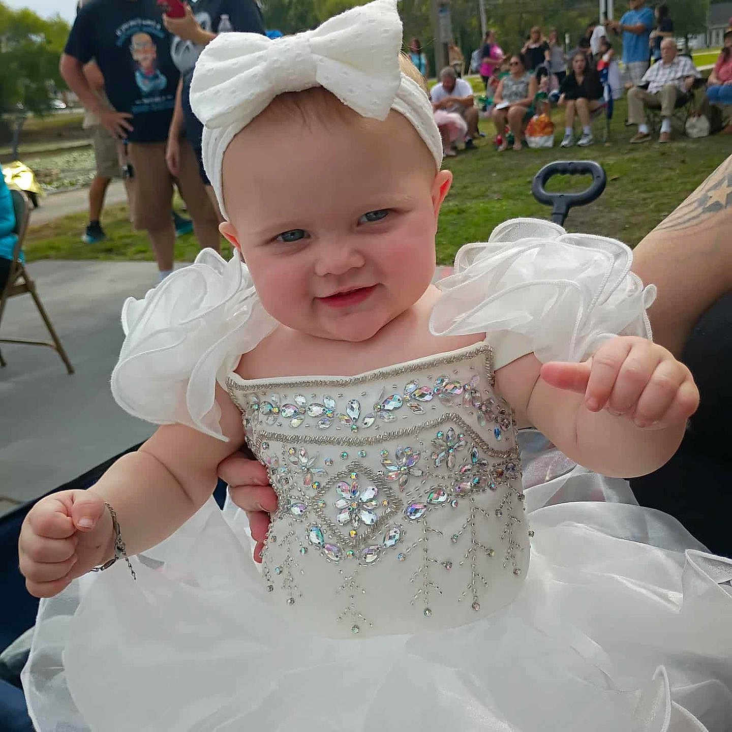 Journey joined the competition — help win amazing prizes! baby, bow, celebration, child, crowd, cute, dress, event, fashion, grass, group, headband, holding, outdoor, park, people, person, smiling, summer, white_dress