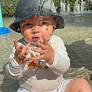 Andrea participe au concours pour gagner de l'argent avec cette photo : toddler, child, water, hat, bucket_hat, swimsuit, animal_print, playing, outdoor, pool, water_droplets, sunlight, reflection, summer, fun, sitting, cute, baby, face, hands
