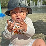 toddler, child, water, hat, bucket_hat, swimsuit, animal_print, playing, outdoor, pool, water_droplets, sunlight, reflection, summer, fun, sitting, cute, baby, face, hands