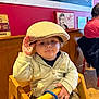 Oakley joined the competition — help win amazing prizes! toddler, child, hat, flat_cap, high_chair, wooden_chair, indoor, cafe, red_wall, vintage_artwork, person, clothing, seated, hand, expression, floor, casual, young_child, portrait, baby