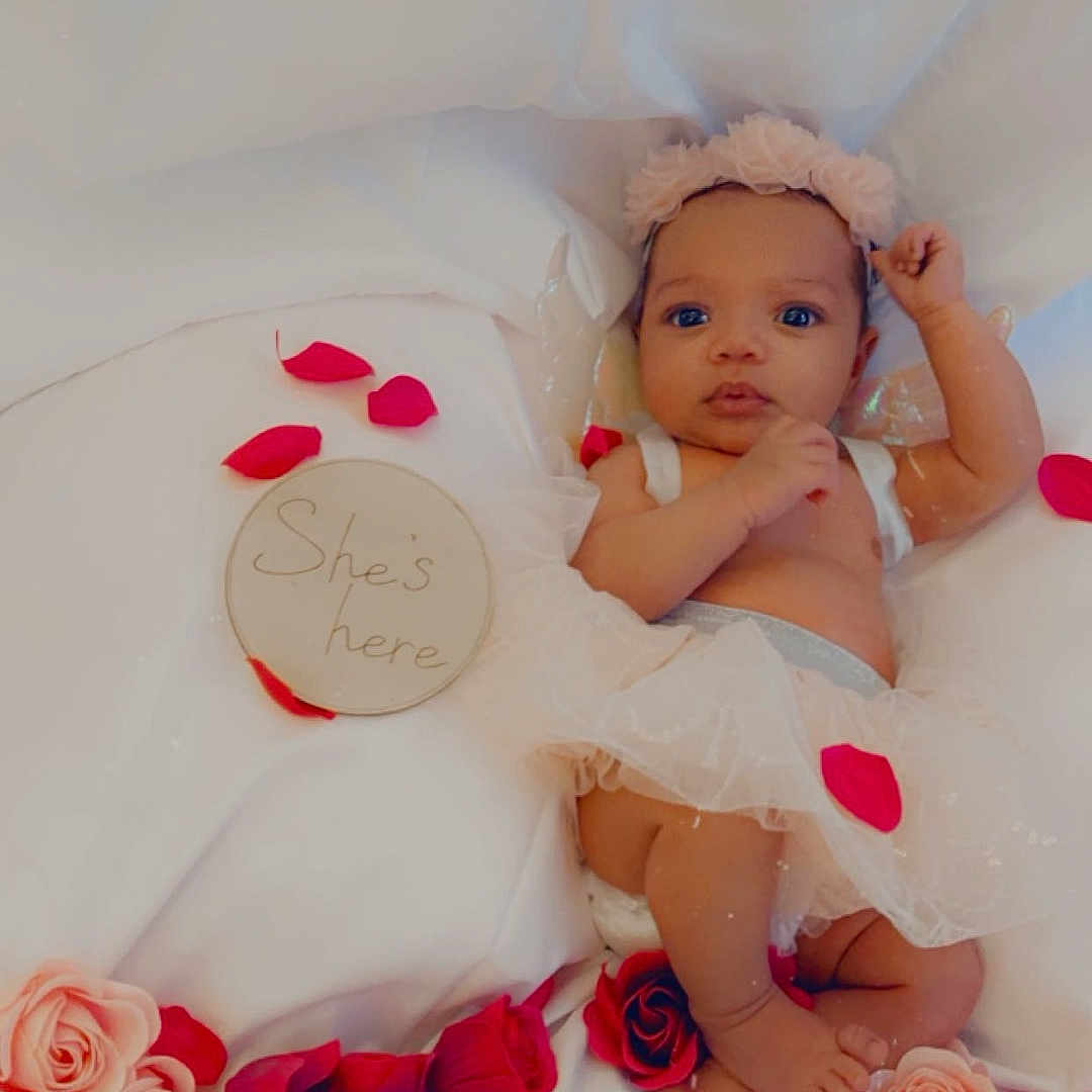 Sariyah is registered to the contest to win money with this photo: announcement, baby, celebration, cute, decorative, feet, flower_headband, hands, infant, lying_down, newborn, pink, portrait, red, rose_petals, sign, skin, soft_lighting, tutu, white_fabric